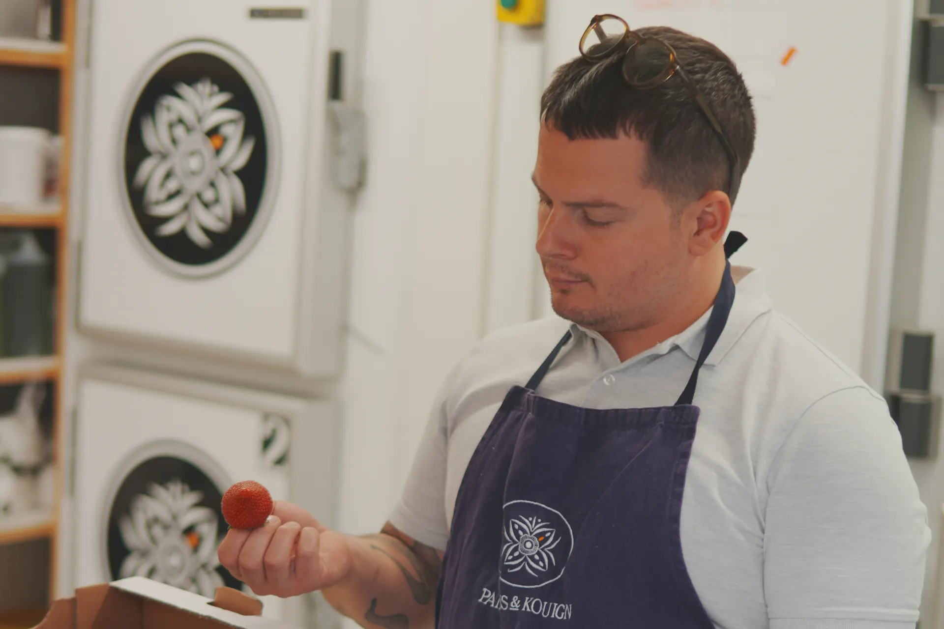 Cuisinier en tablier bleu marine examinant une fraise lors de la réception d’une livraison