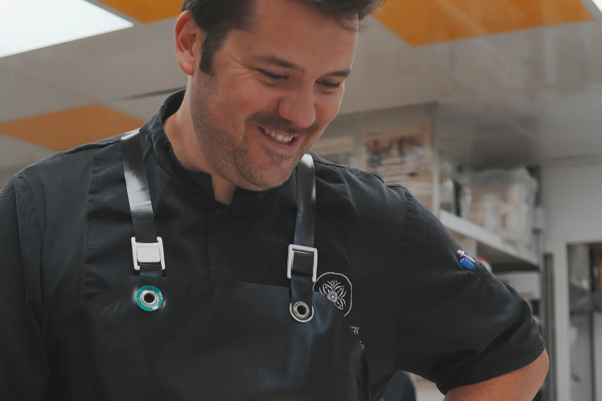 Chef souriant en veste et tablier noirs dans un laboratoire de pâtisserie