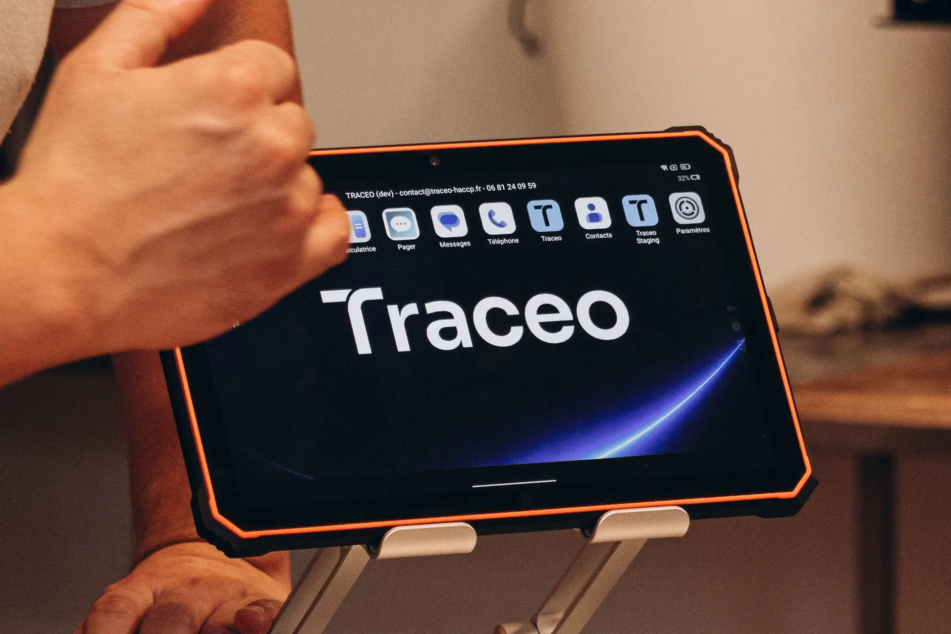 Tablette durcie affichant le logo Traceo sur un support, au-dessus d’une rangée de sandwichs sur un plan de travail en inox